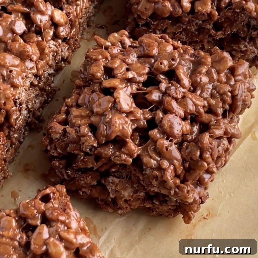 A perfectly square piece of dark chocolate Rice Krispie treat, showcasing its chewy texture and visible mini chocolate chips.
