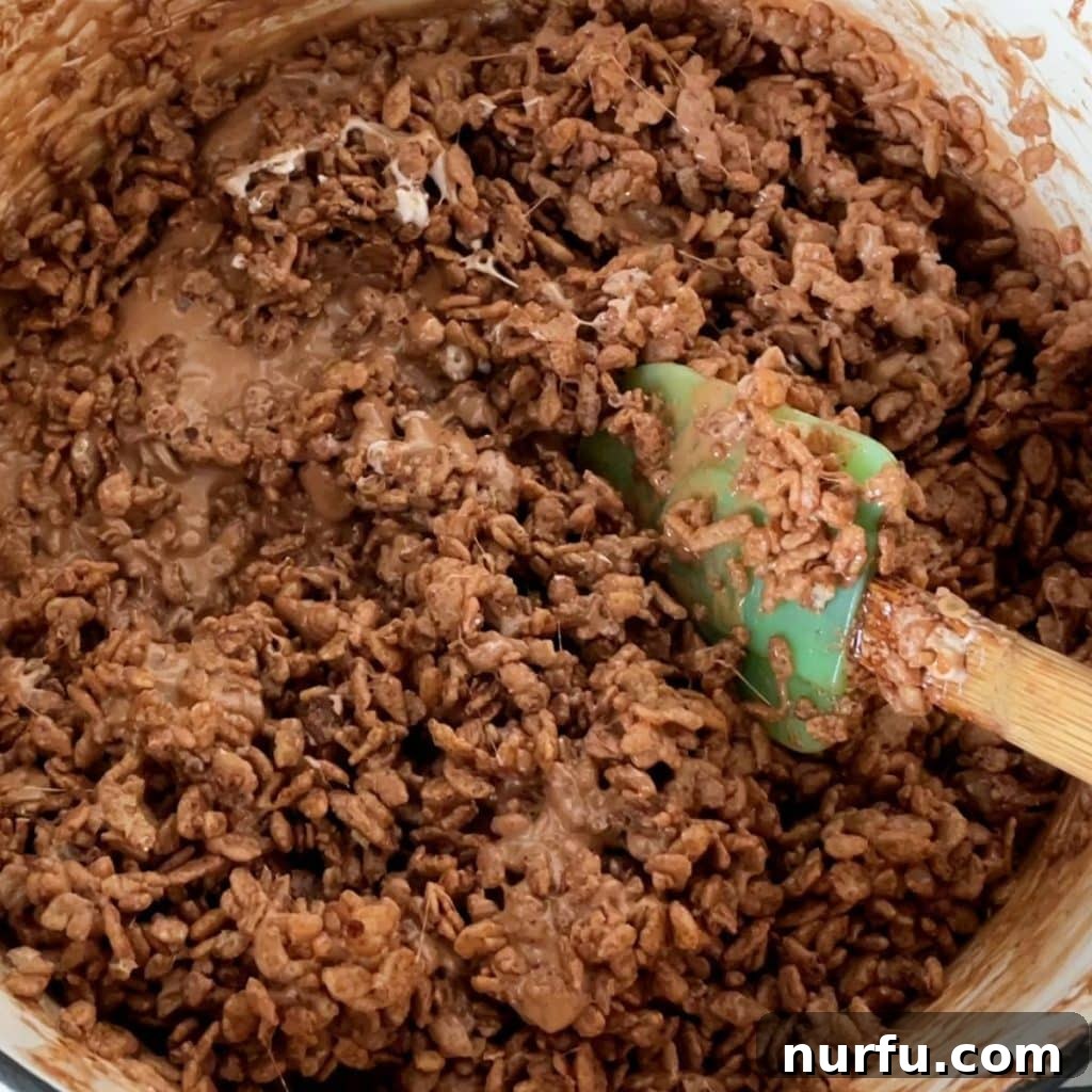 Cocoa Rice Krispies cereal being stirred into a rich, melted chocolate and marshmallow mixture in a saucepan, ensuring even coating.