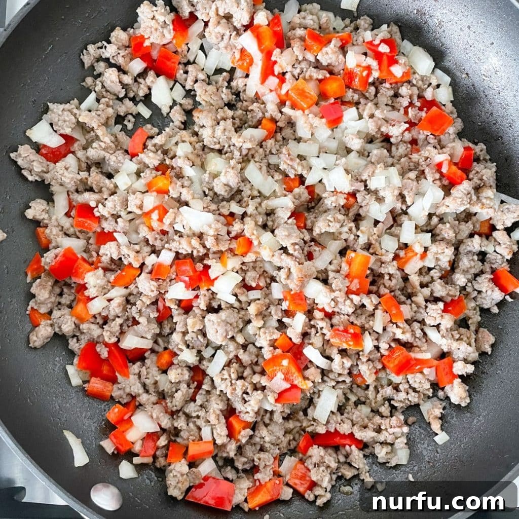 Golden Bisquick Breakfast Delight 4 A large skillet containing crumbled, browned breakfast sausage mixed with diced red bell pepper and onion, gently sautéing.