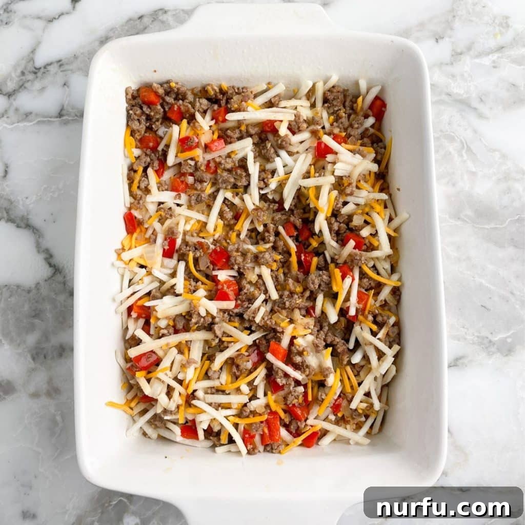 Golden Bisquick Breakfast Delight 5 A 9x13 inch casserole dish filled with a mixture of cooked sausage, diced peppers and onions, and half of the shredded cheese, thoroughly mixed.