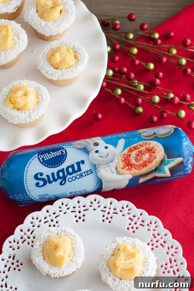 Eggnog Cookie Cups A roll of Pillsbury sugar cookie dough rests beside a plate of freshly baked eggnog cookie cups, showcasing the convenience of ready-made ingredients for holiday baking.