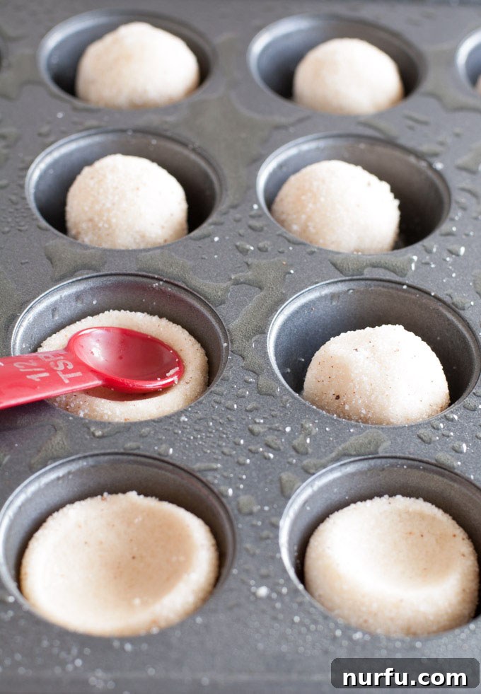 Eggnog sugar cookie cups Raw sugar cookie dough balls, coated in a cinnamon-sugar mixture, are pressed into a mini muffin pan, ready for baking to form perfect cookie cups.