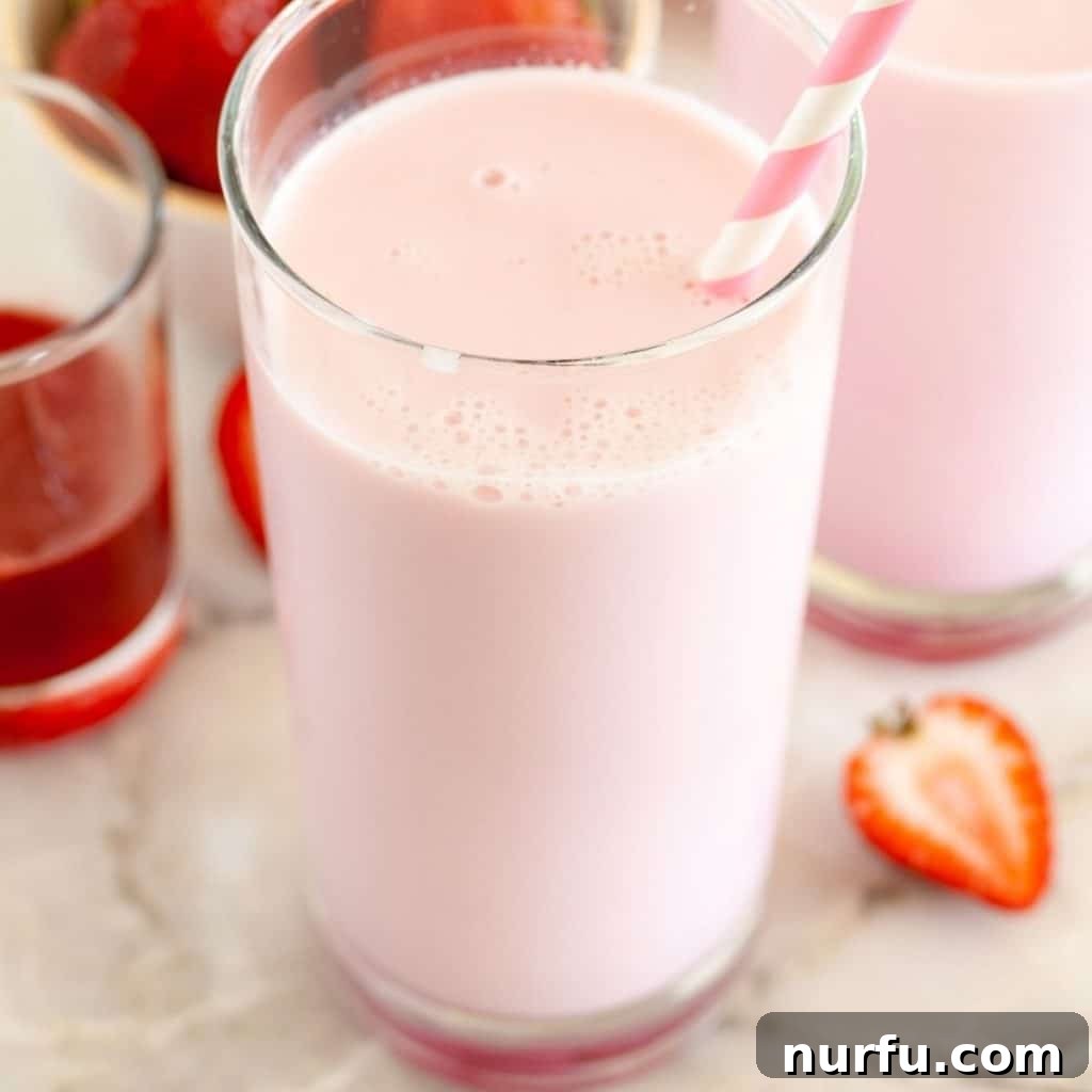 Two glasses of pink strawberry milk, garnished with fresh strawberries, looking deliciously refreshing and inviting.