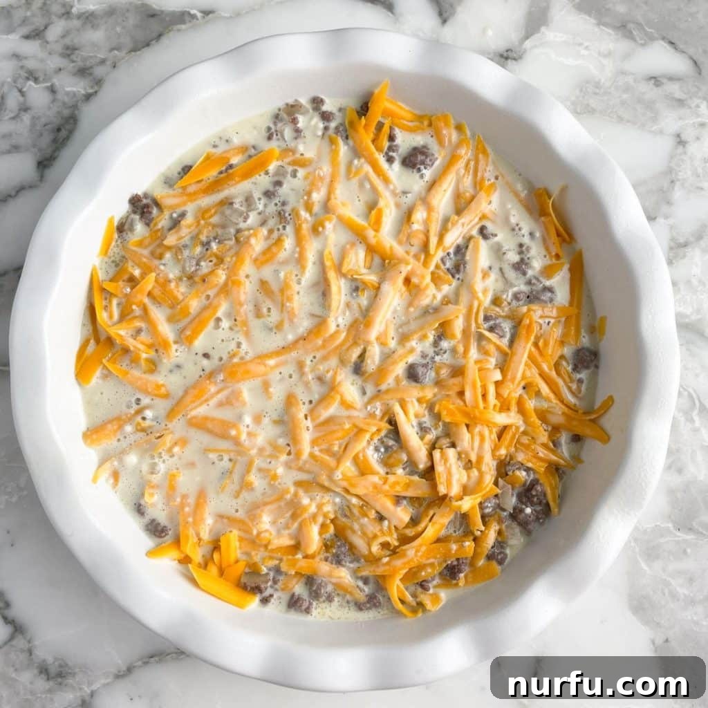 The Bisquick Cheeseburger Pie in a pie plate, with the egg and Bisquick mixture poured over the ground beef and shredded cheese, ready for baking.