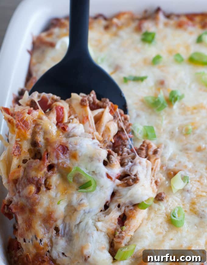 Serving Ground Beef Pasta Casserole A spatula scooping a generous portion of cheesy ground beef pasta casserole, highlighting the layers.