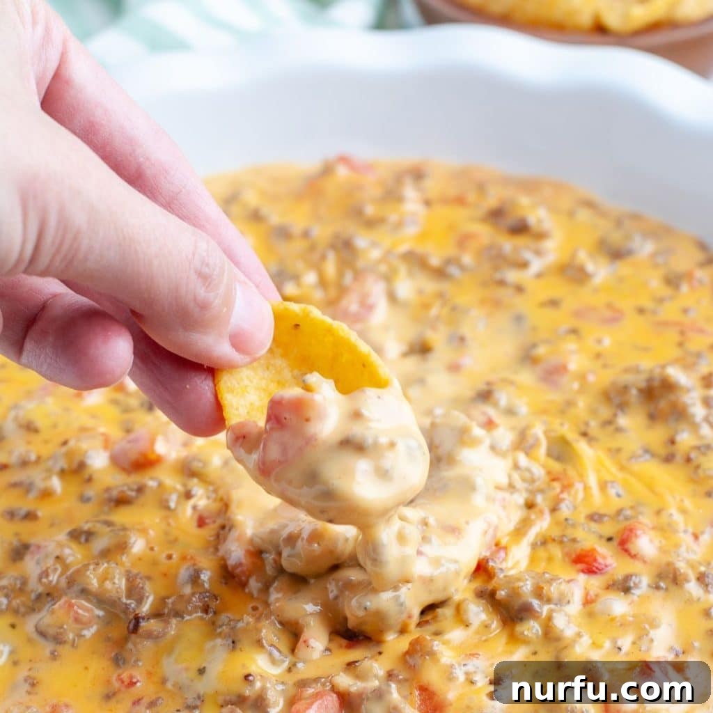 Creamy Velveeta Sausage Dip 2 Hand holding ship with cheesy dip.