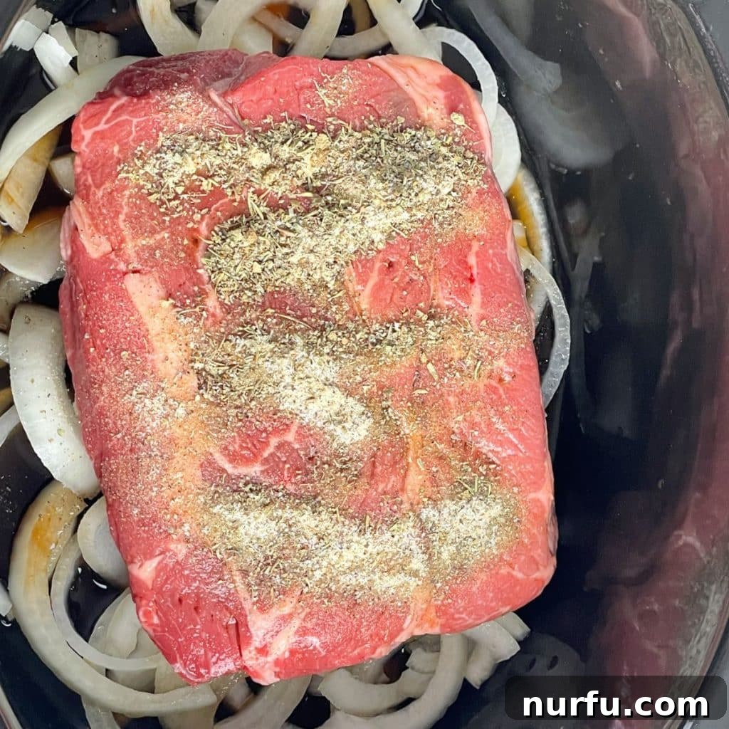 Melt-in-Your-Mouth Slow Cooker Beef 5 A seasoned chuck roast resting on sliced onions in a slow cooker, covered in a rich spice mixture, ready for slow cooking.