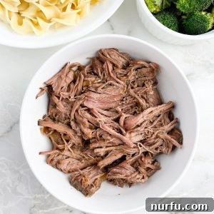 A bowl of tender, juicy shredded beef, served alongside a bowl of egg noodles and fresh steamed broccoli florets.