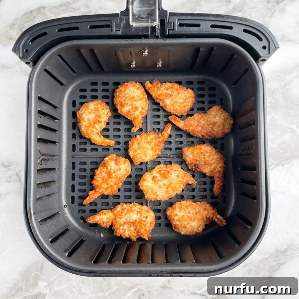 Crispy Air Fryer Frozen Coconut Shrimp 4 Crispy golden coconut shrimp perfectly cooked and resting inside an air fryer basket.