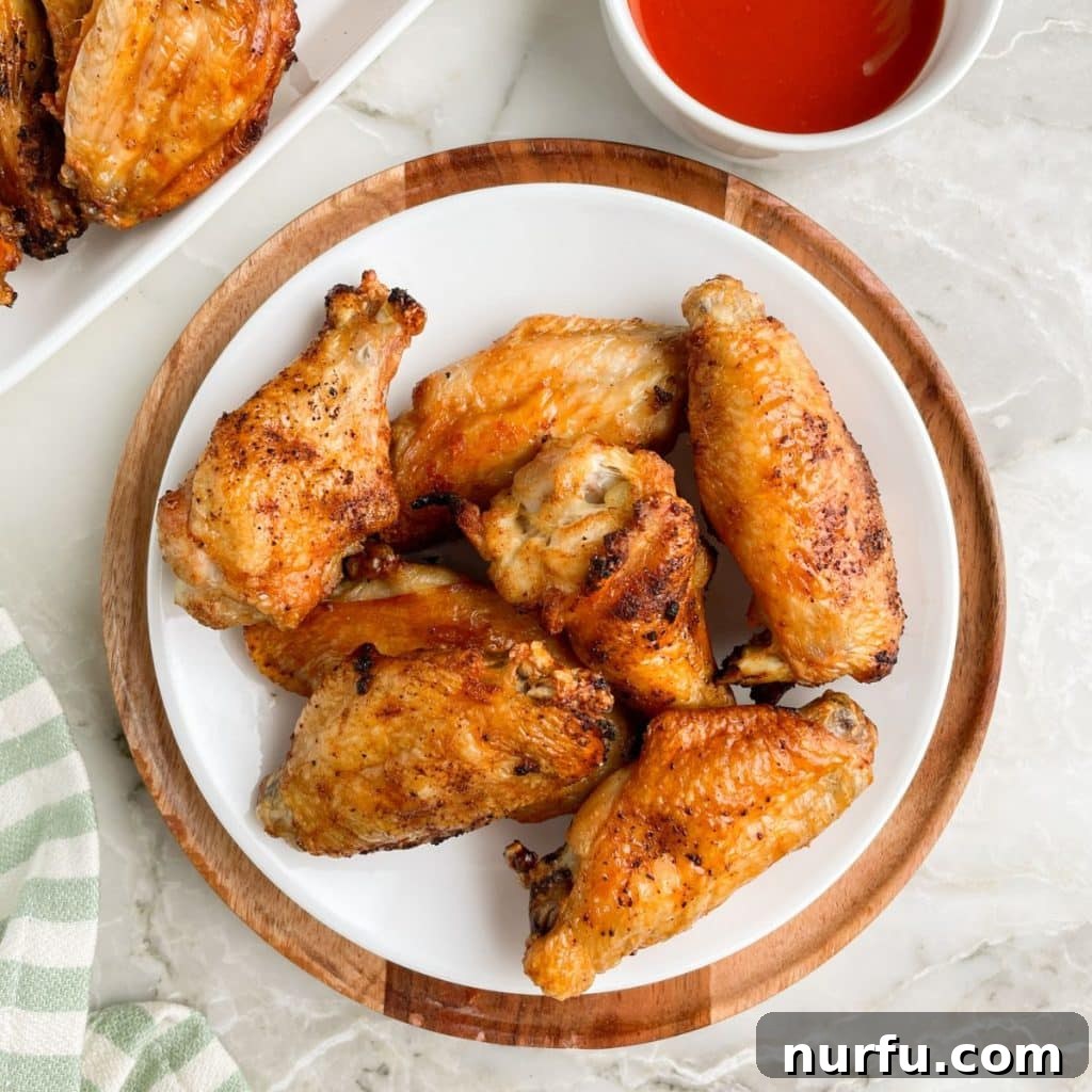 A beautifully arranged plate of golden-brown, crispy baked chicken wings served with a small bowl of dipping sauce, perfect for a party appetizer.