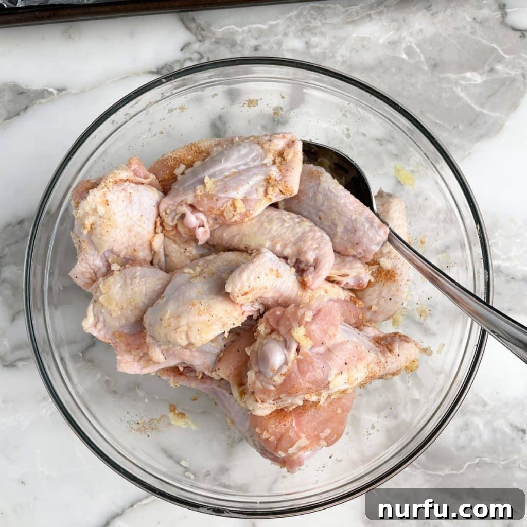 A large mixing bowl filled with uncooked chicken wings, glistening with melted butter and savory seasonings, tossed and ready for baking.