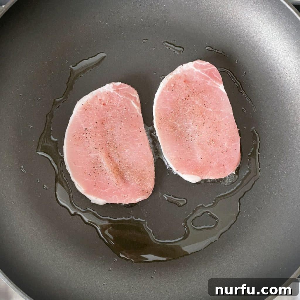 Thin pork chops sizzling vigorously in a hot skillet, vividly showcasing the early stages of searing with a desirable crust beginning to develop.