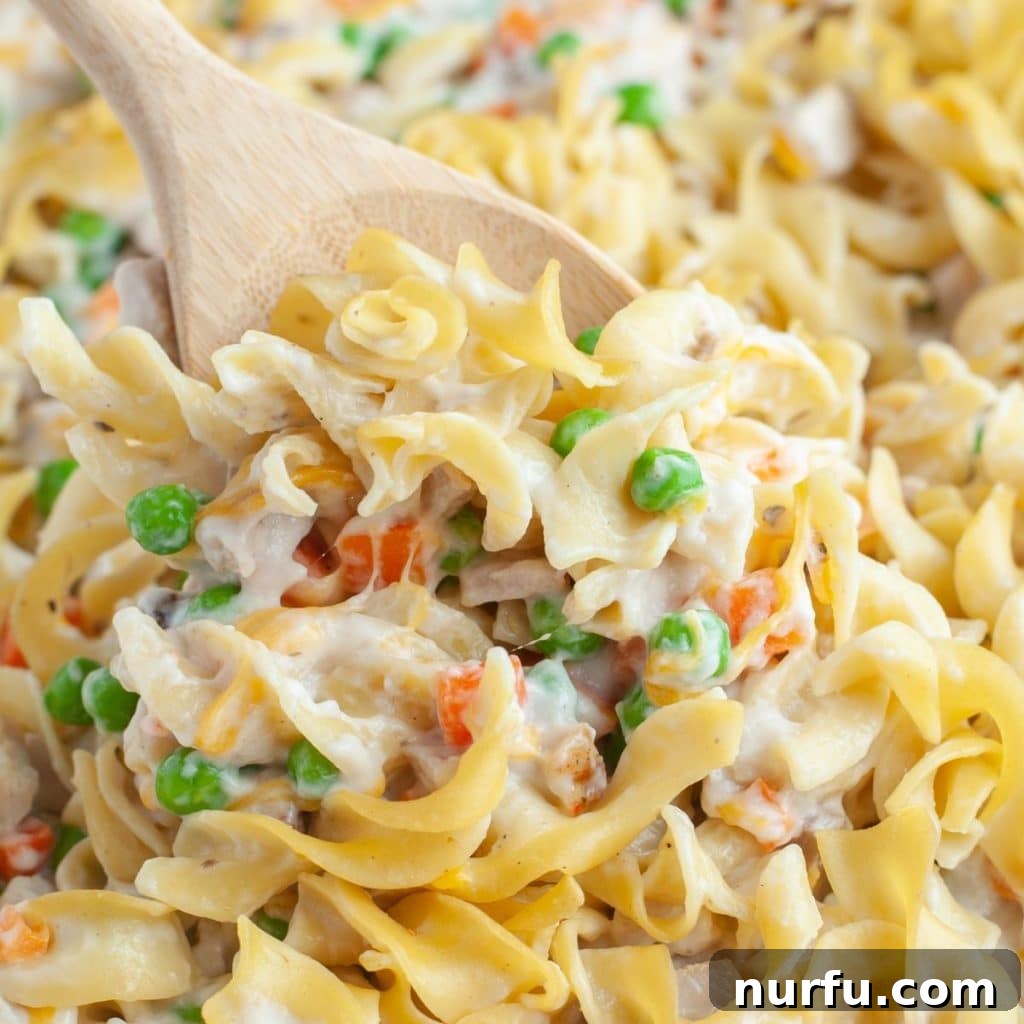 Hearty Pork Casserole 2 A wooden spoon serving a delicious pork noodle casserole with a golden-brown top.