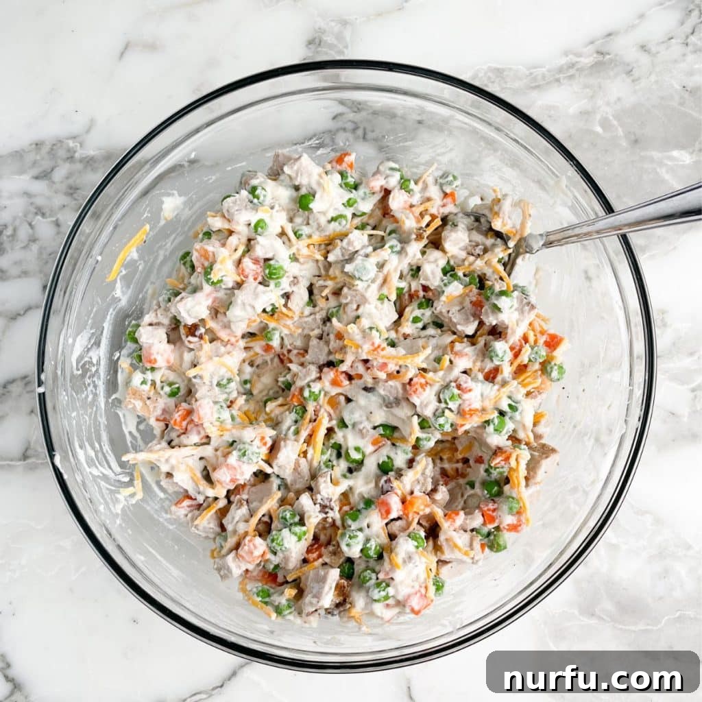 Hearty Pork Casserole 4 A large mixing bowl containing a creamy mixture of diced pork, cream of mushroom soup, peas and carrots, and shredded cheddar cheese, ready to be combined.