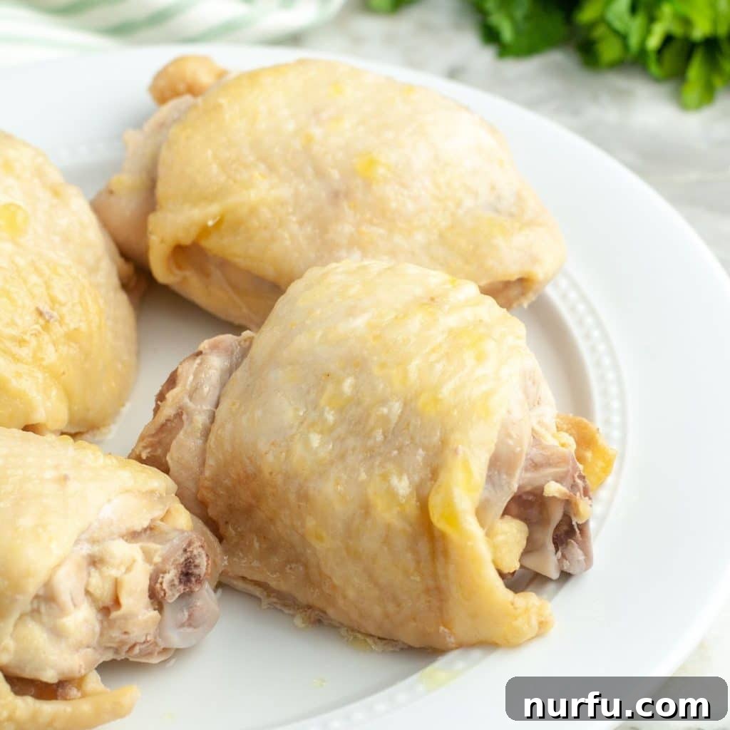 The Secret to Perfectly Tender Boiled Chicken Thighs 2 Boiled chicken thighs on a plate, garnished with fresh herbs.