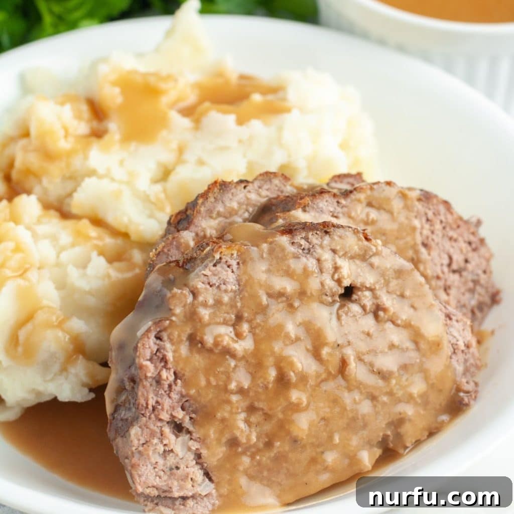 Hearty slices of homemade meatloaf topped with luscious brown gravy and served alongside creamy mashed potatoes on a white plate, symbolizing the perfect comfort meal.