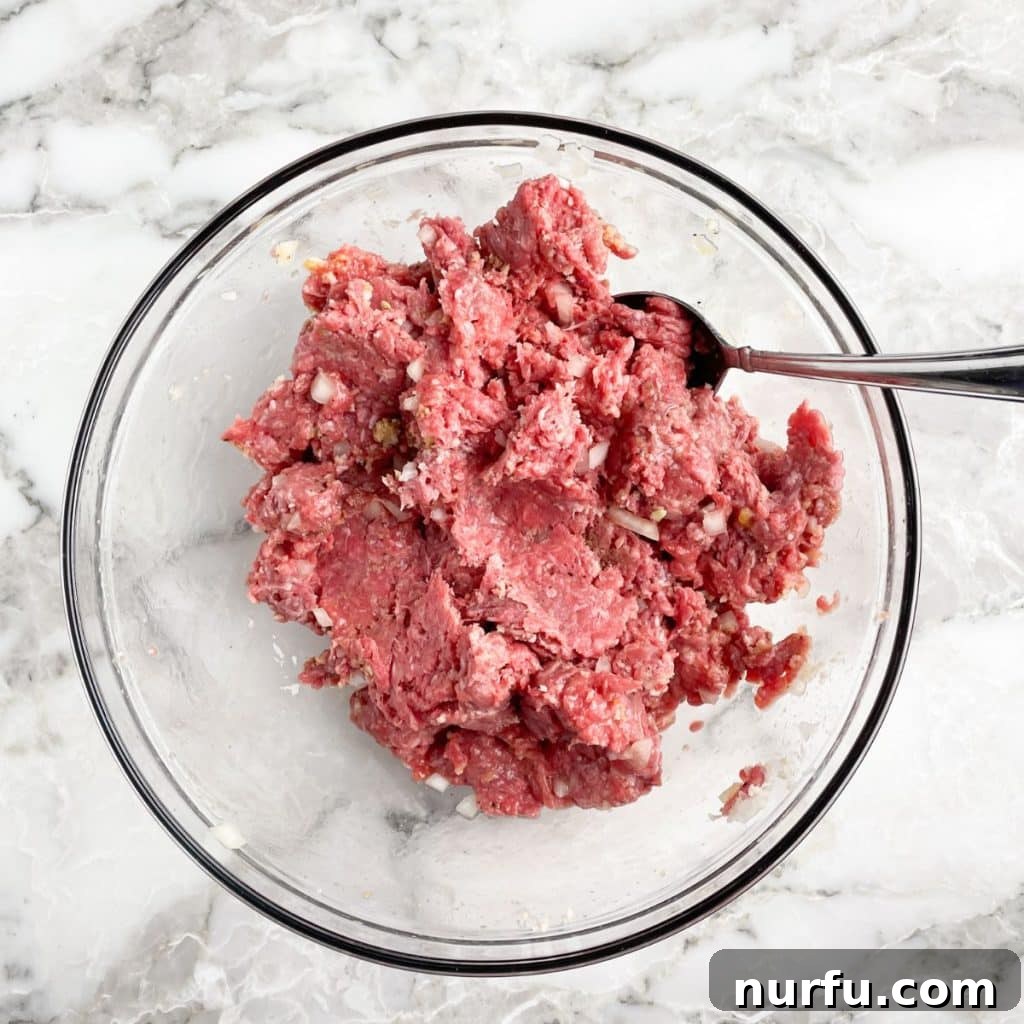 Large mixing bowl containing ground beef and various seasonings, ready to be combined for a homemade meatloaf recipe.