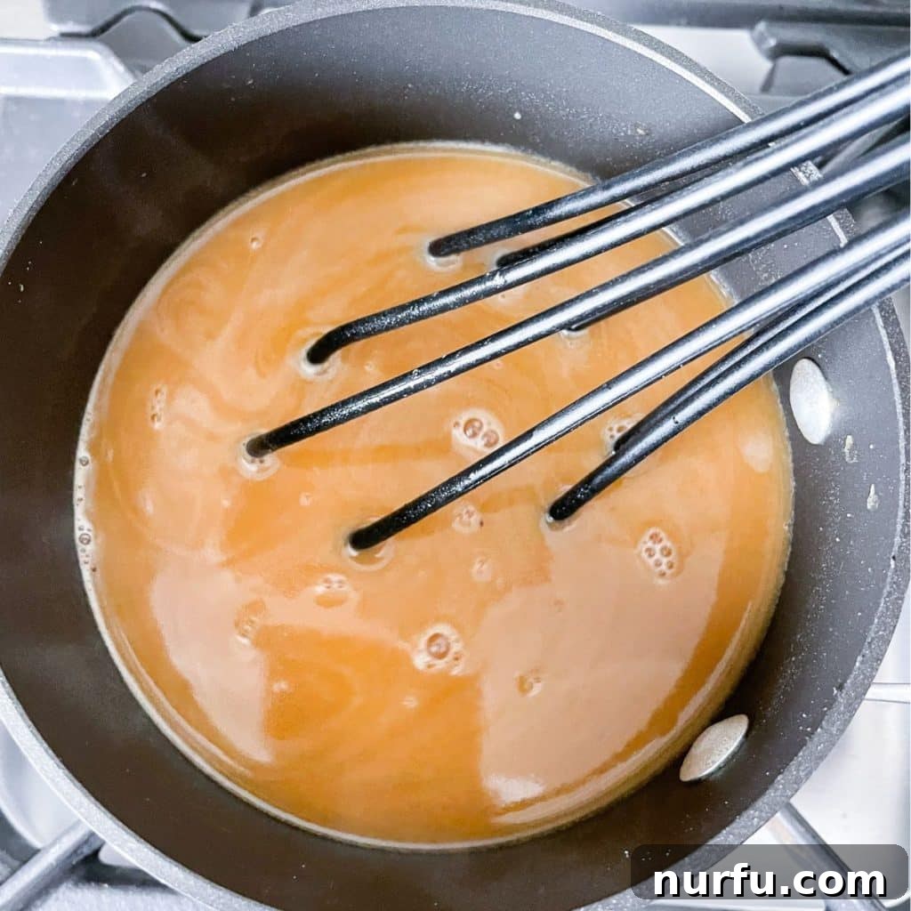 A saucepan on the stove with brown gravy being whisked, showcasing the rich, smooth texture of the homemade sauce.
