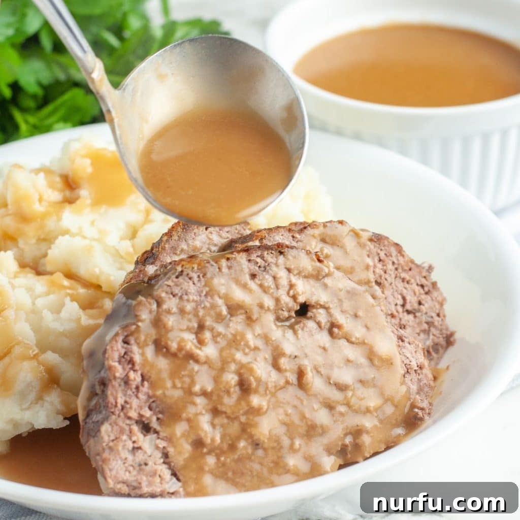 Perfectly sliced meatloaf served with a generous amount of rich brown gravy and a side of fluffy mashed potatoes, ready to be enjoyed.