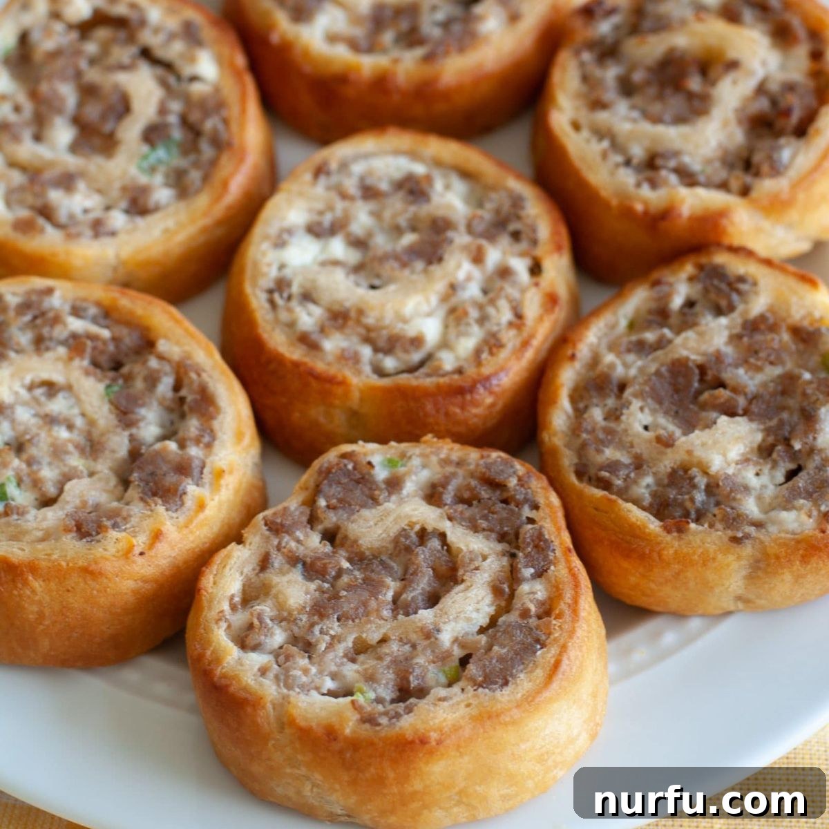 Brinner Bonanza: 31 Recipes for Anytime 6 Golden-brown Sausage and Cream Cheese Pinwheels arranged on a serving plate, showing their spiraled layers of dough and savory filling.