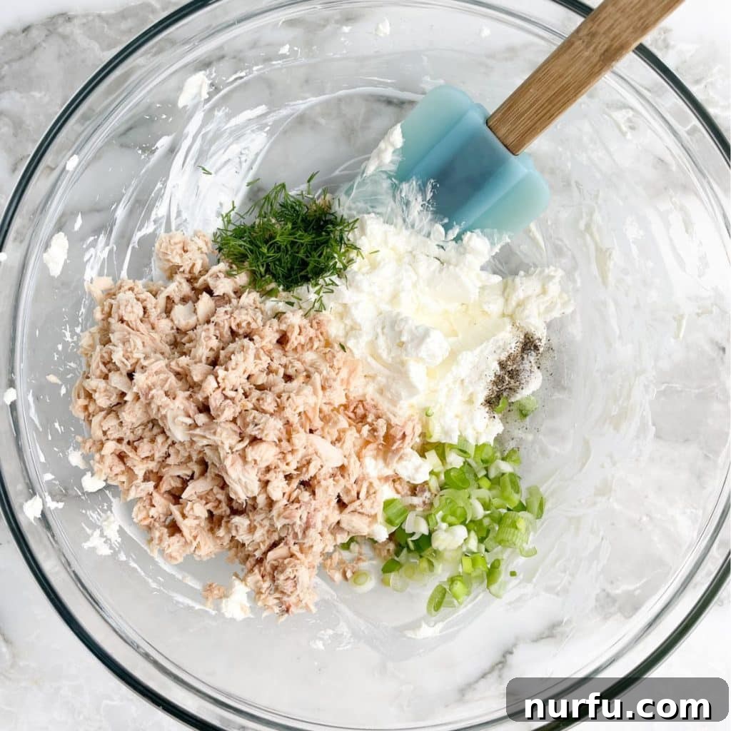 Bowl with flaked salmon, cream cheese, fresh dill, and green onions mixed together, mid-preparation.