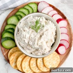 Bowl of salmon dip with sliced cucumbers, radish, and crackers.