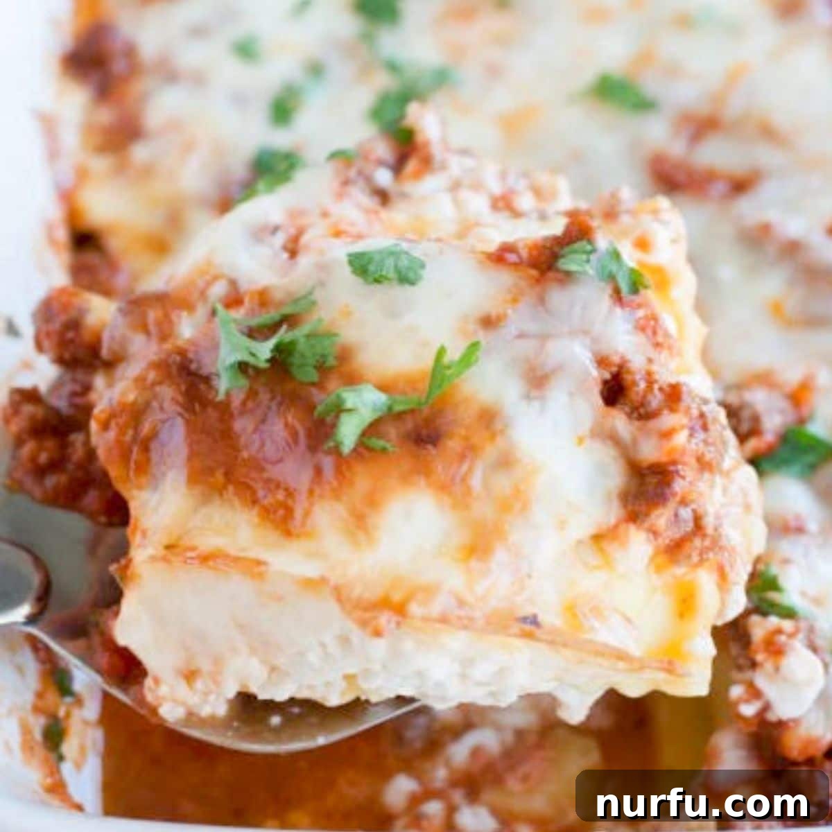 Hearty Ravioli Lasagna Bake 2 Delicious Baked Ravioli Lasagna in a baking dish, with a serving spoon ready to scoop a portion.