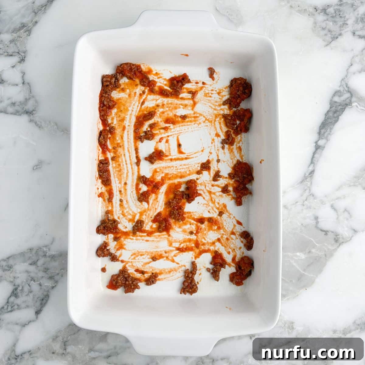 Hearty Ravioli Lasagna Bake 4 The first layer of flavorful meat sauce spread evenly in a rectangular baking dish, forming a delicious foundation.