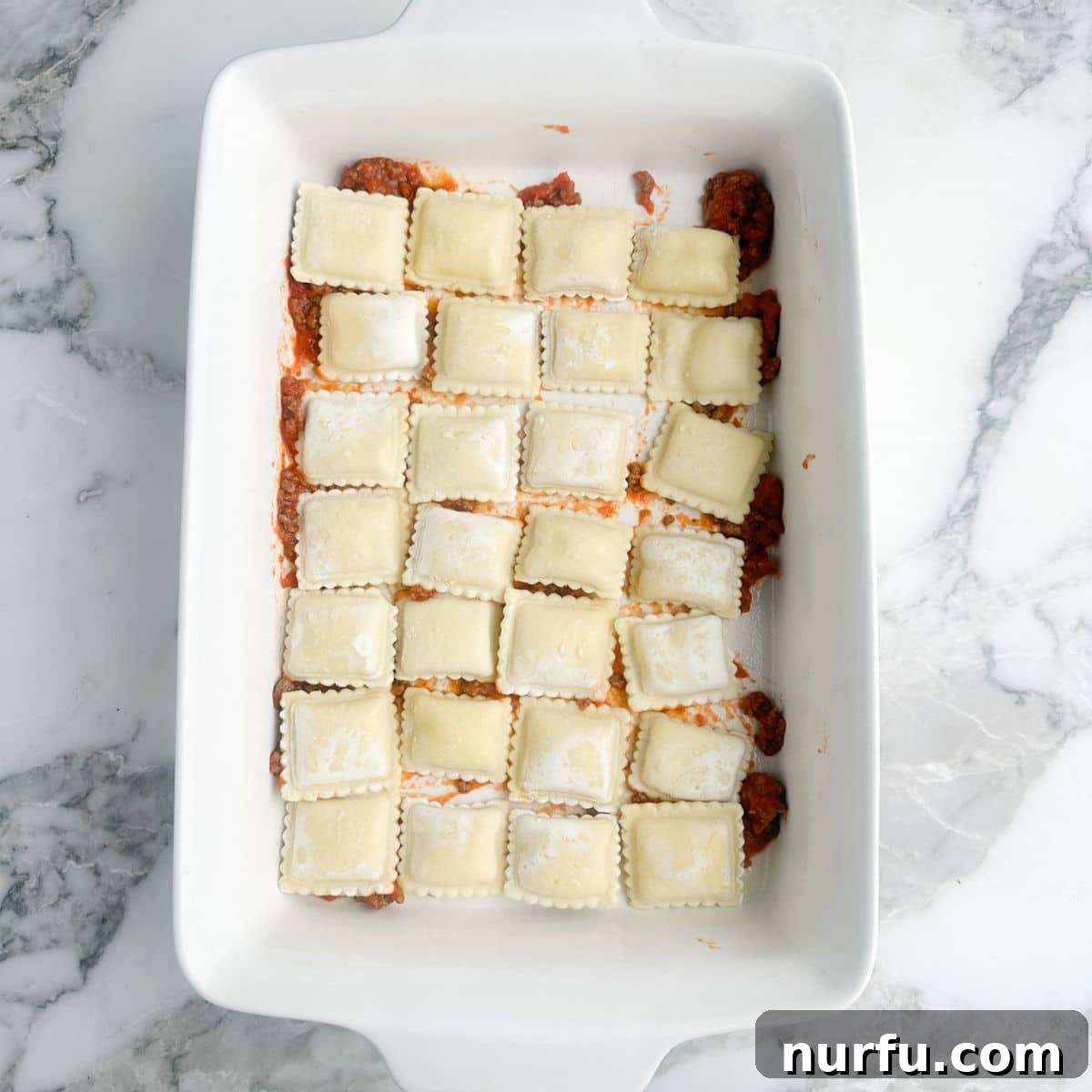 Hearty Ravioli Lasagna Bake 5 A neat single layer of uncooked ravioli perfectly arranged over the meat sauce, ready for the next layer of cheese mixture.