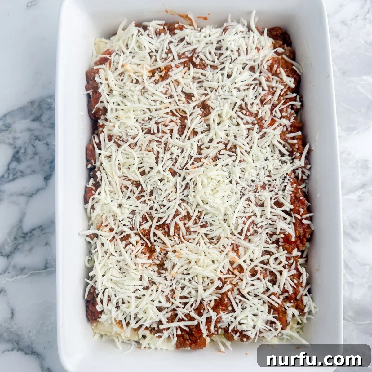 Hearty Ravioli Lasagna Bake 7 The assembled Baked Ravioli Lasagna ready for baking, showcasing its rich layers of meat sauce and abundant shredded cheese on top.