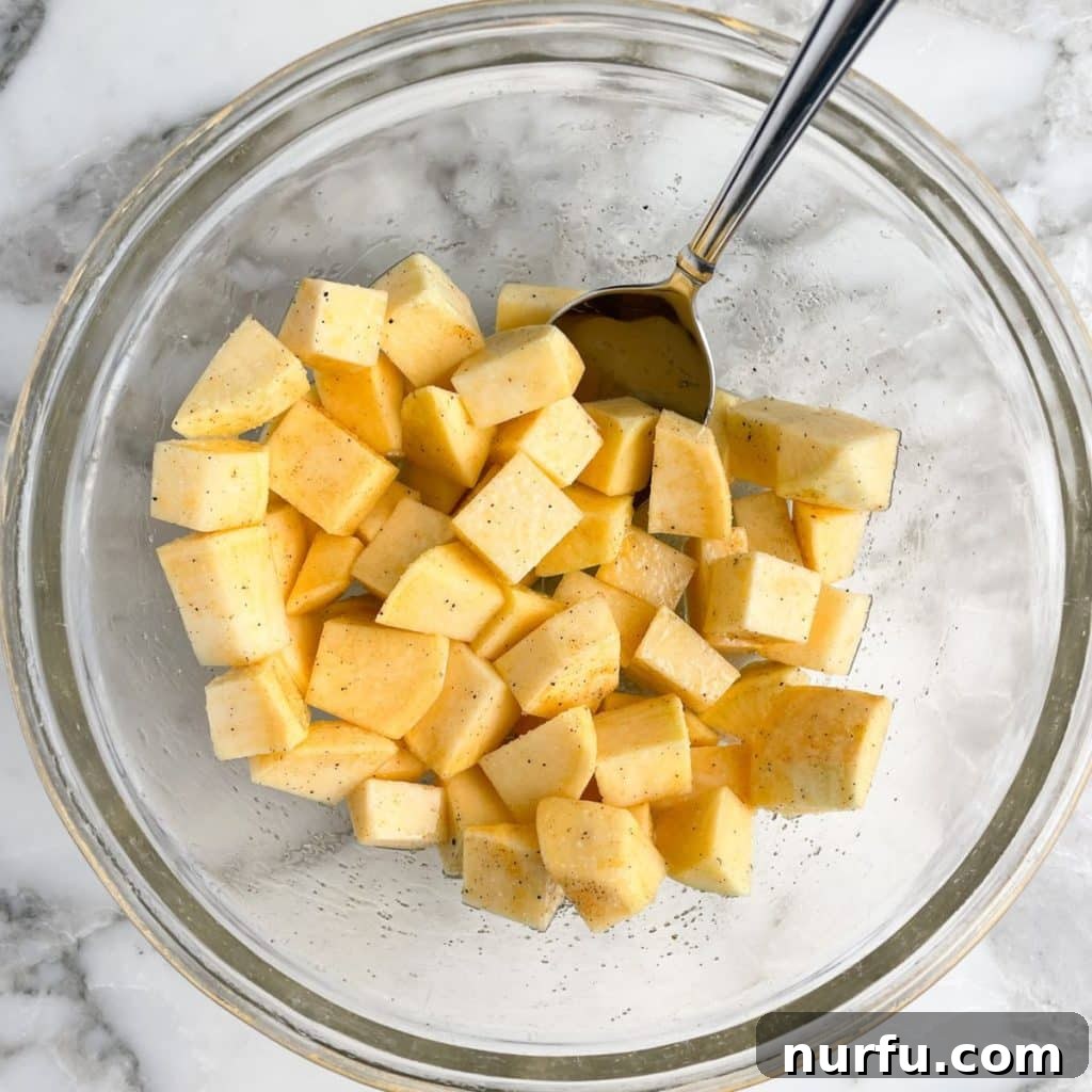 Golden Roasted Rutabaga 4 A close-up shot of uniformly cubed rutabaga in a mixing bowl, generously coated with olive oil and spices, with a spoon nestled within, ready for roasting.