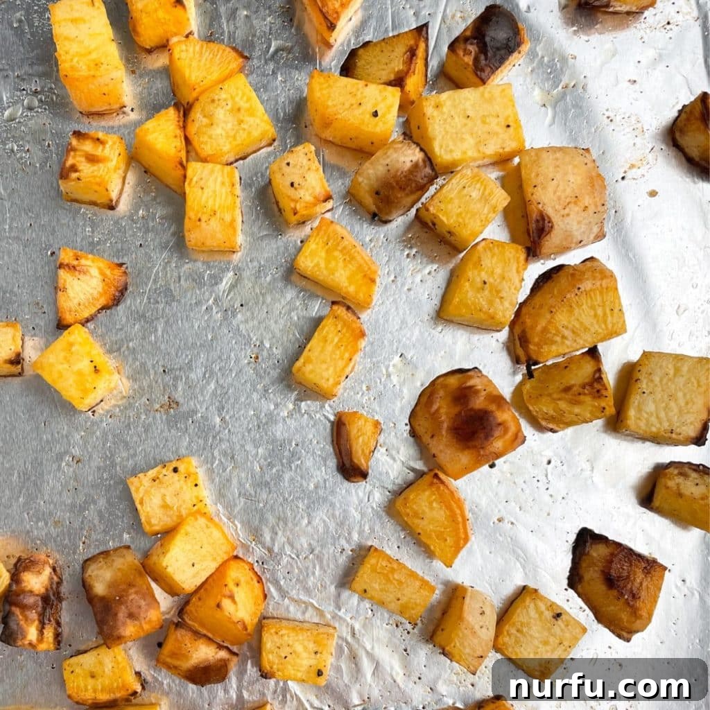 Golden Roasted Rutabaga 5 Freshly roasted rutabaga cubes spread evenly on a foil-lined baking sheet, showcasing their golden-brown edges and tender appearance straight from the oven.