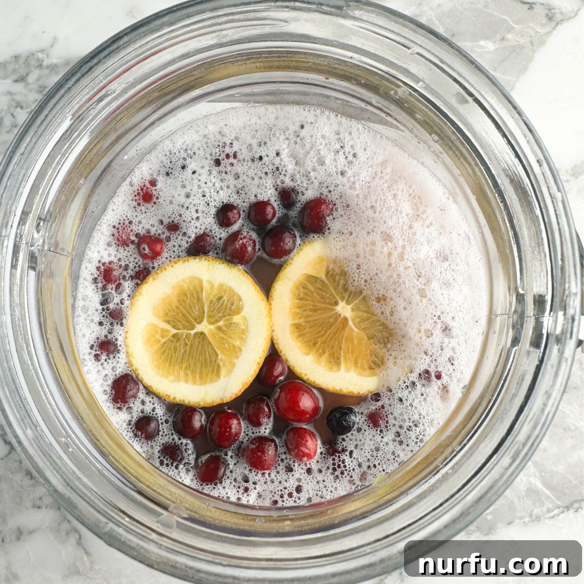 Virgin Holiday Punch 4 A large jar filled with vibrant holiday punch, garnished with fresh cranberries and orange slices, ready to be served.
