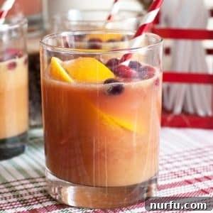 A beautifully garnished glass of festive holiday punch, featuring a slice of orange and a straw, ready for sipping.