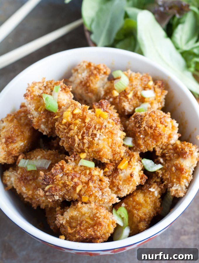 Baked honey garlic turmeric chicken A bowl filled with golden-brown, crispy baked honey garlic turmeric chicken bites, garnished with green onions and ready to be enjoyed.