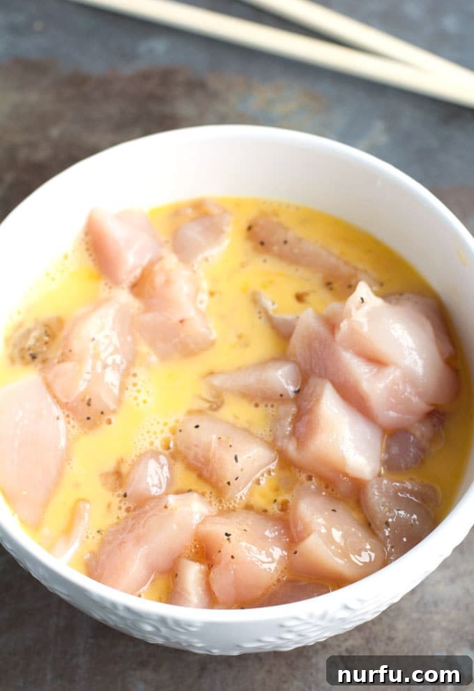 Preparing chicken for baking Chicken pieces being dipped into a bowl of beaten egg mixture, ensuring a complete coating before breading.