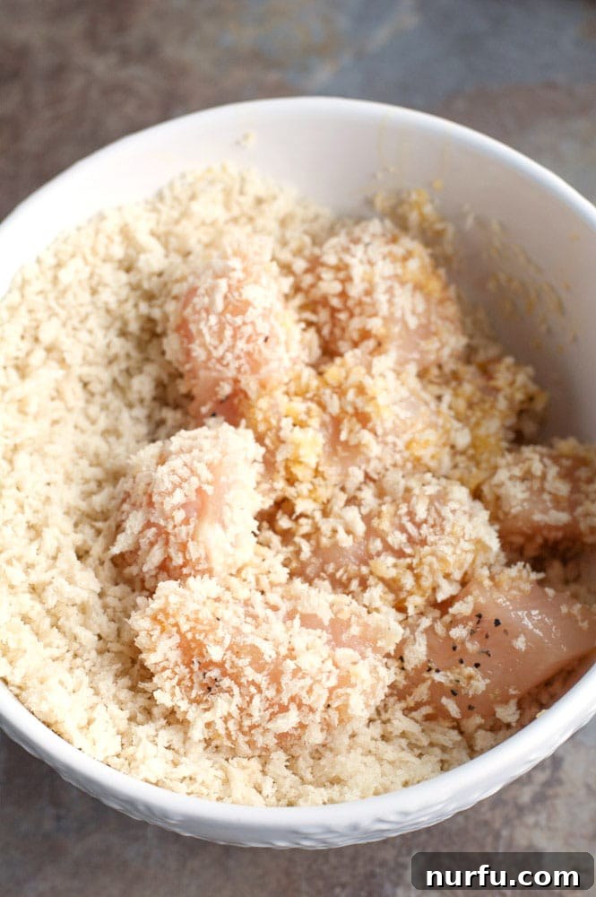 Chicken coated in Panko breadcrumbs Chicken pieces fully coated in crispy Panko breadcrumbs, ready to be placed on a baking sheet.