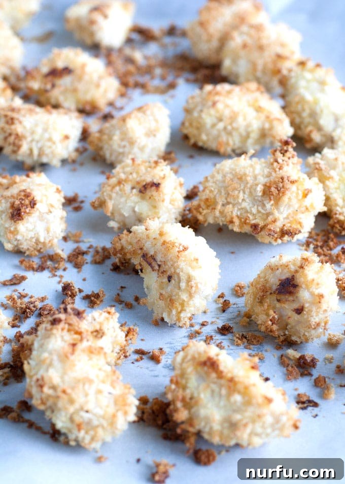 Baked crispy chicken nuggets Golden-brown, perfectly baked chicken nuggets cooling on a baking sheet lined with parchment paper.