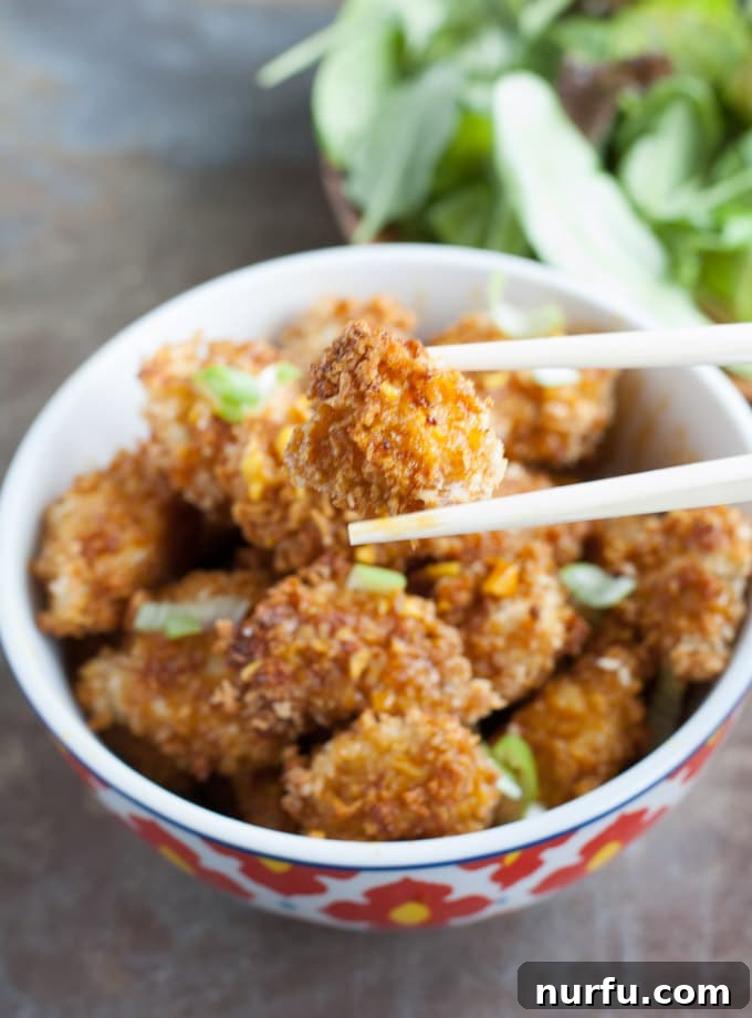 Honey garlic turmeric chicken bite with chopsticks A single piece of baked honey garlic turmeric chicken, held by chopsticks, showcasing its crispy texture and golden sauce.