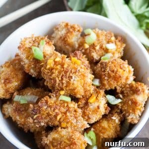 A bowl filled with golden-brown, crispy baked honey garlic turmeric chicken bites, garnished with green onions and ready to be enjoyed.