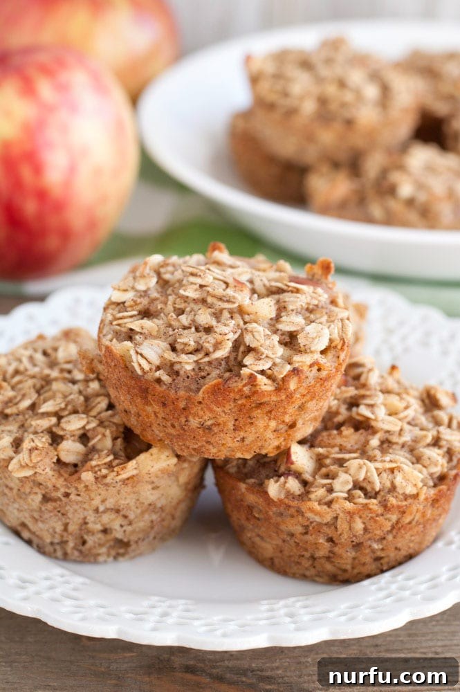 apple cinnamon baked oatmeal cups A plate with three apple cinnamon baked oatmeal cups and fresh apples in the background, showcasing a healthy and convenient breakfast option.