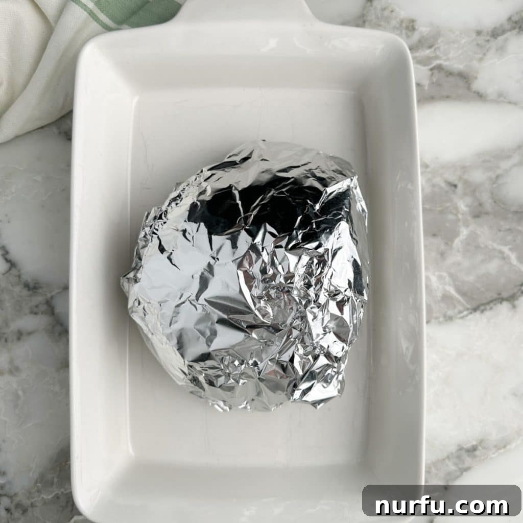 How Long To Bake Ham Fresh Precooked and Frozen 4 Ham wrapped in foil within a baking dish, ready for the oven.