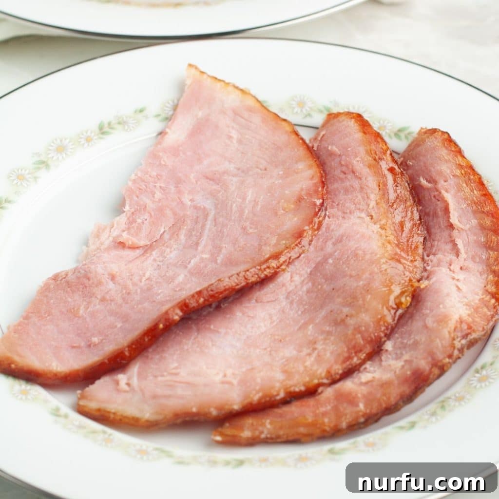 How Long To Bake Ham Fresh Precooked and Frozen 6 Perfectly sliced baked ham on a plate, showcasing its tenderness.