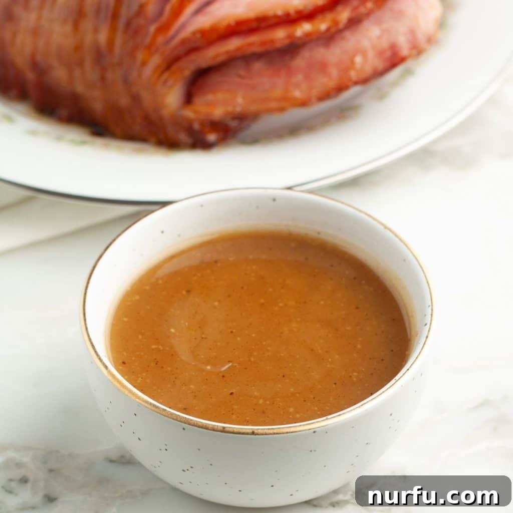 Tropical Pineapple Ham Glaze 2 Bowl of sweet and sticky pineapple ham glaze, with a perfectly cooked, glistening ham in the background, ready for serving at a festive table.