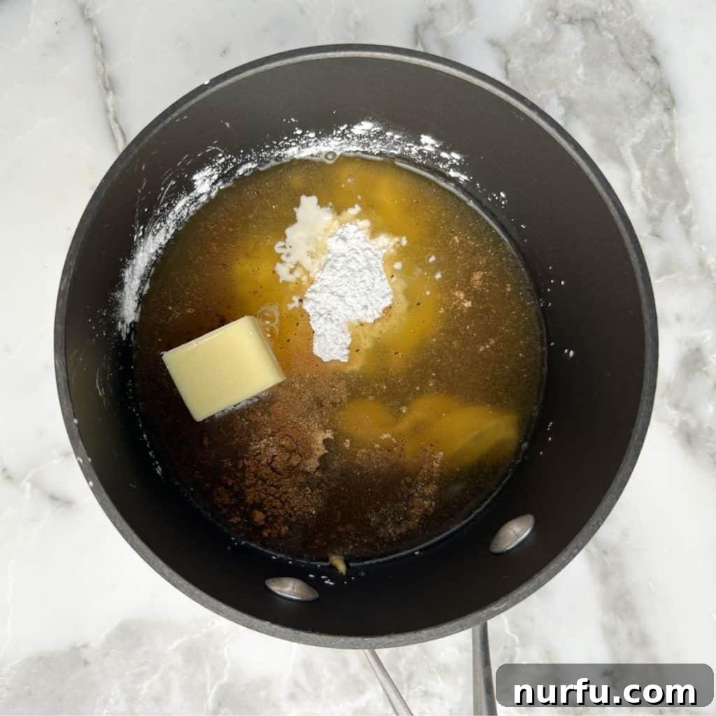 Tropical Pineapple Ham Glaze 4 Close-up of a saucepan on a stovetop, containing pineapple juice, brown sugar, cornstarch, butter, and mustard, being whisked together before heating.