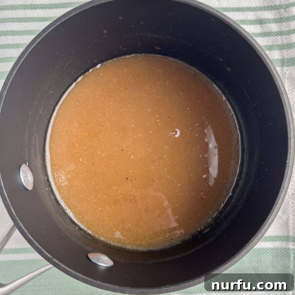 Tropical Pineapple Ham Glaze 5 A simmering saucepan filled with the golden-brown ham glaze, which has thickened to a perfect consistency, ready to be applied.