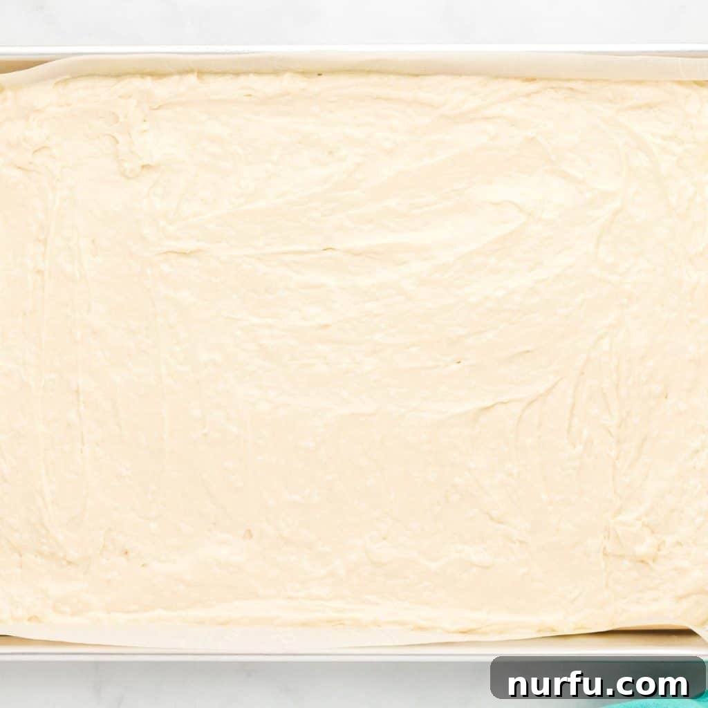 Tropical Coconut Dream Cake 4 A sheet cake pan filled with creamy, white coconut cake batter, perfectly spread and ready for baking, promising a delicious dessert.