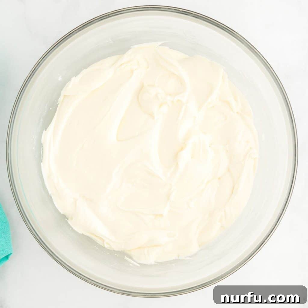 Tropical Coconut Dream Cake 5 A large, pristine bowl filled with freshly made, smooth white cream cheese frosting, ready to be spread onto a cake.