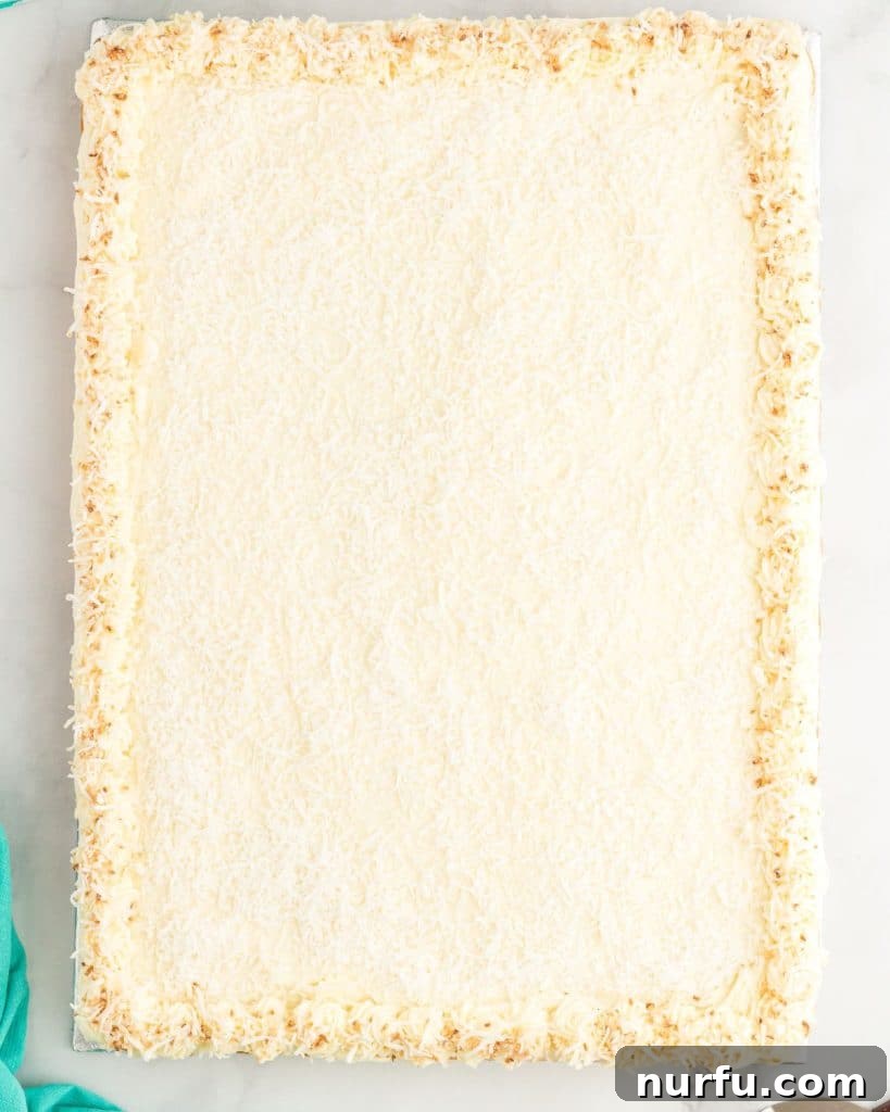 Tropical Coconut Dream Cake 6 A beautifully frosted coconut sheet cake, generously covered with white cream cheese frosting and sprinkled with shredded coconut, showcasing its moist texture.