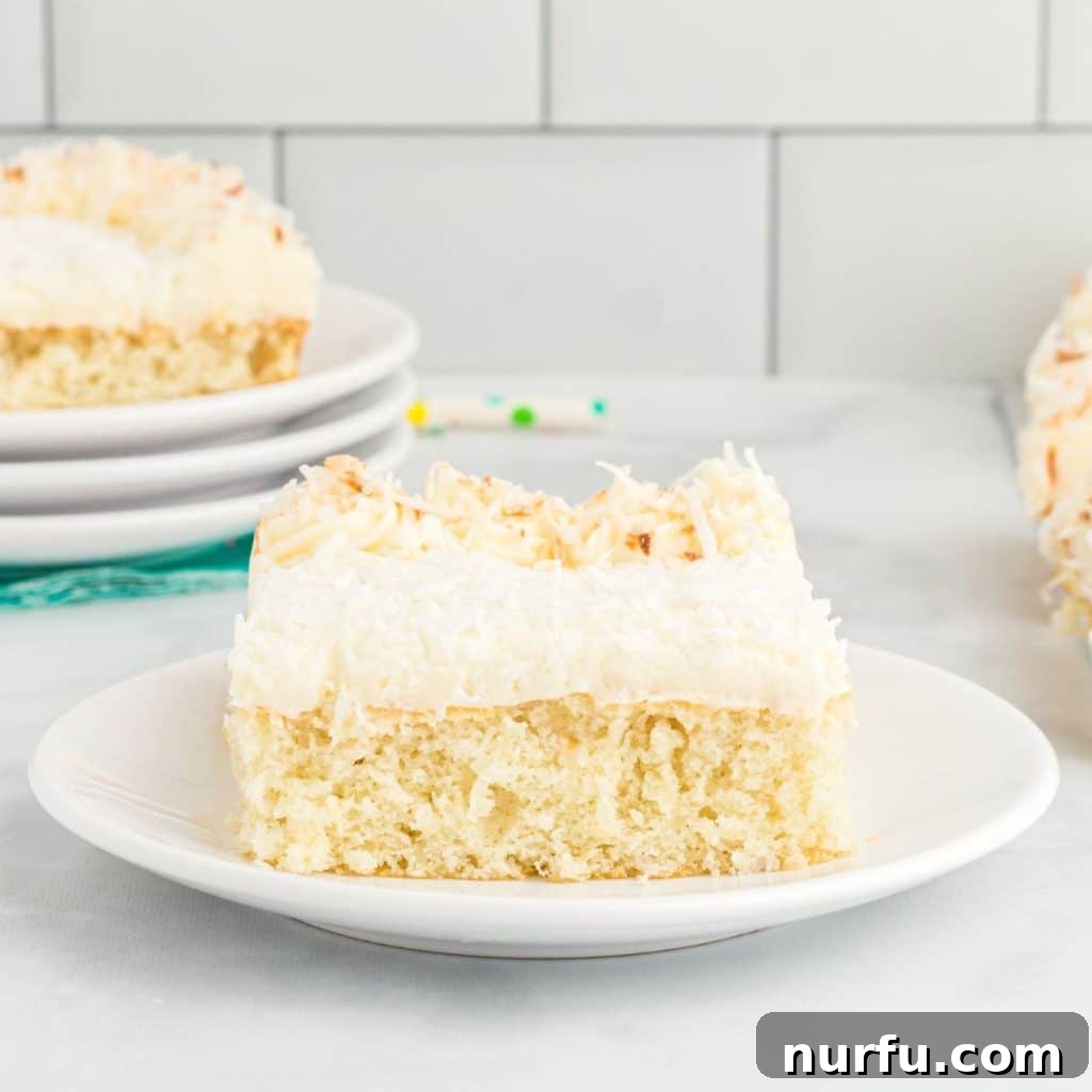 Tropical Coconut Dream Cake 7 A delicious slice of coconut sheet cake, topped with fluffy cream cheese frosting and toasted coconut, presented on a white plate with a fork.